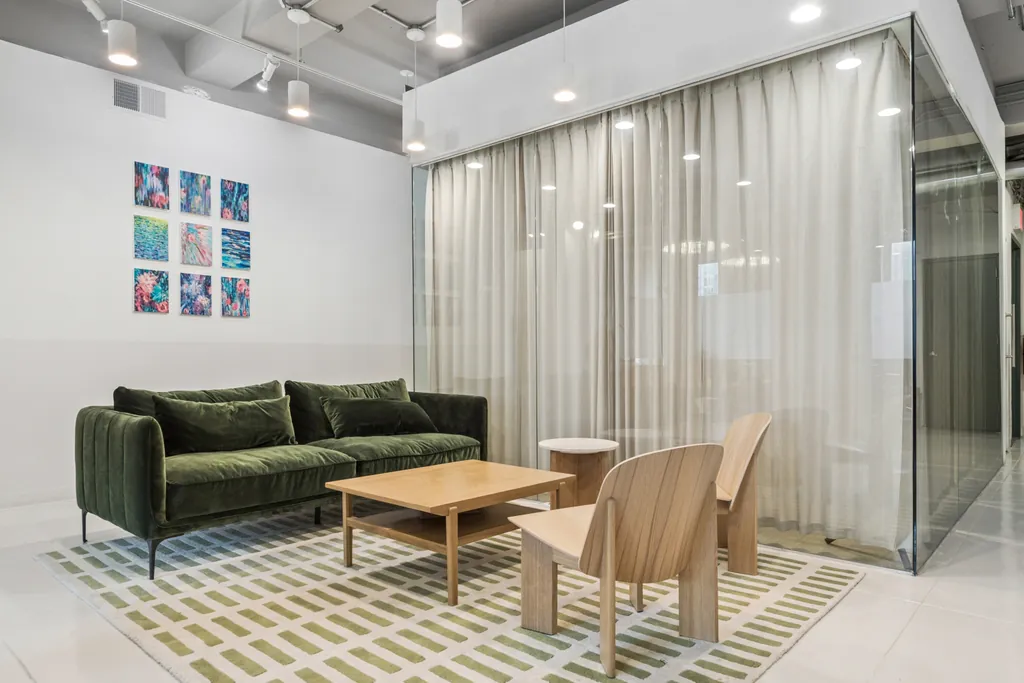 A lounge seating area at The Yard with a green velvet couch, wood furniture, and a glass meeting room